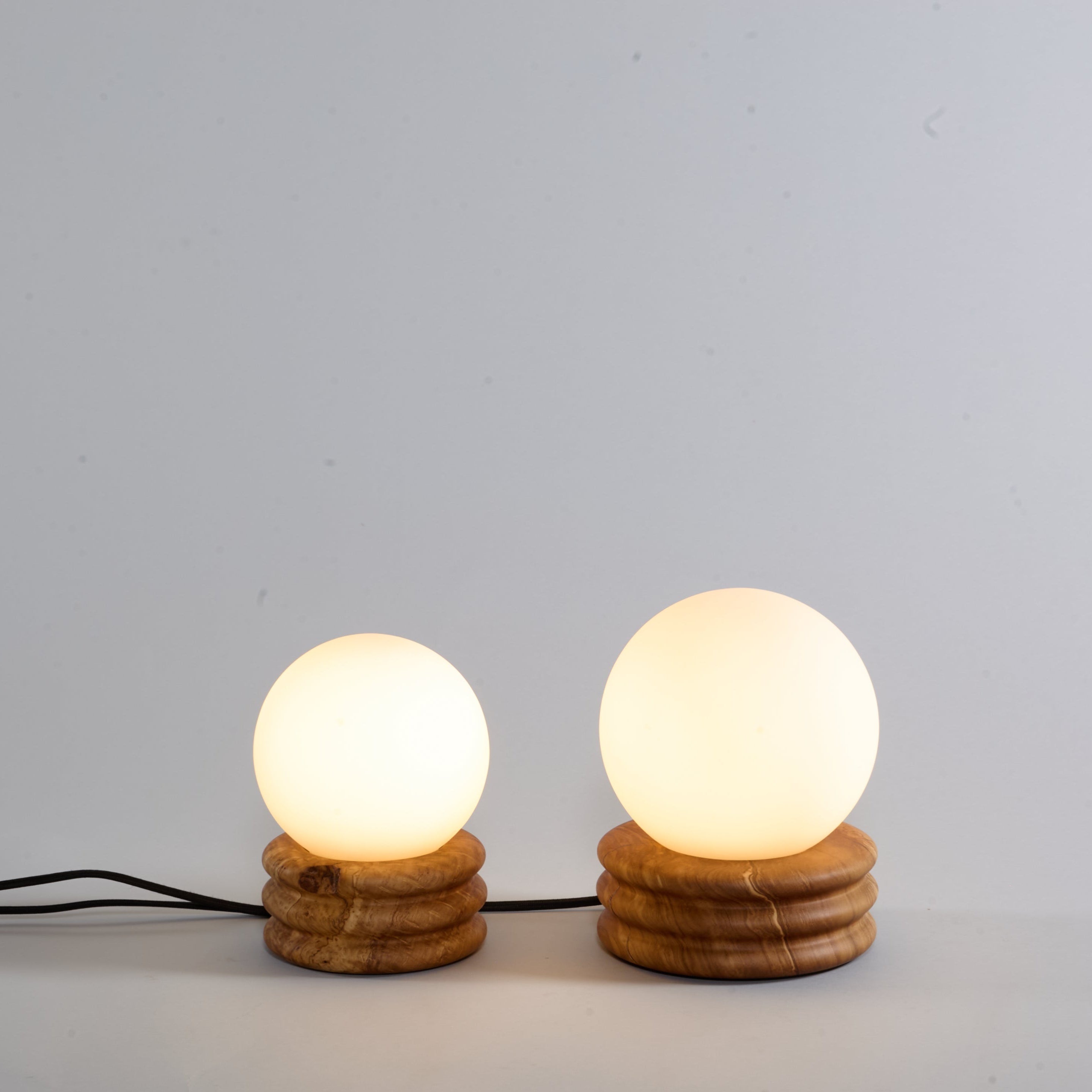 Two small table lamps with round glass shades on wooden bases against a light gray background.